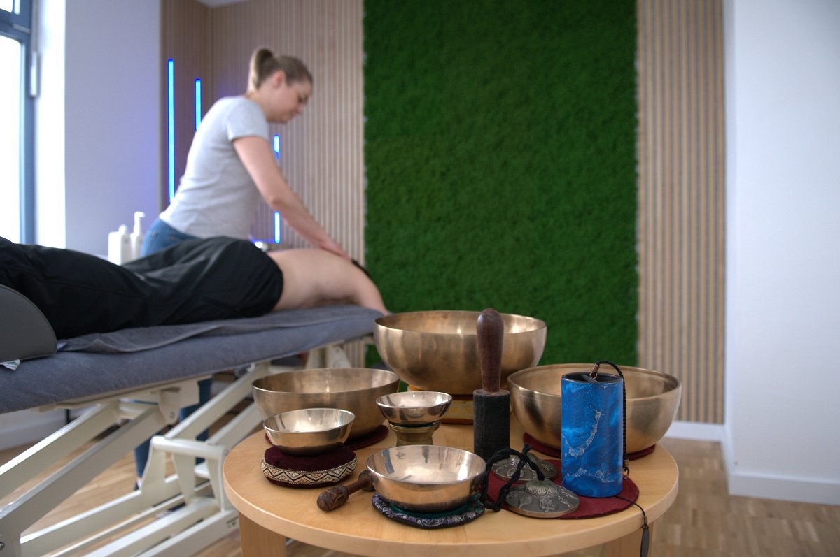 Massage mit Klangschalen vor begrünter Wand